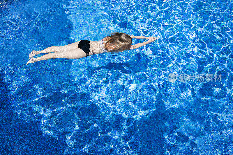 一个十几岁的女孩在一个蓝色的游泳池里用尖尖的手在水下游泳