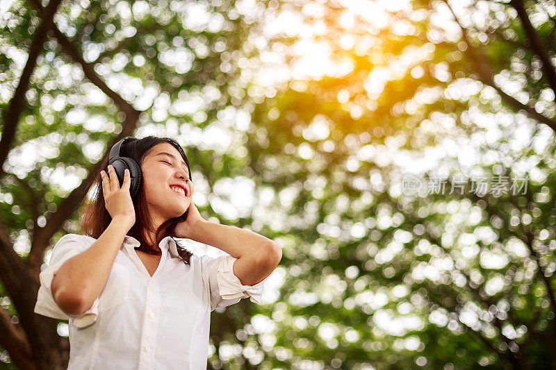 年轻快乐微笑的亚洲女人听音乐耳机在公园
