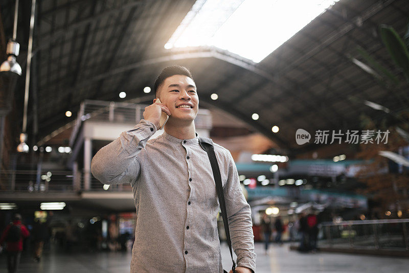 英俊的亚洲男人在火车站用手机。