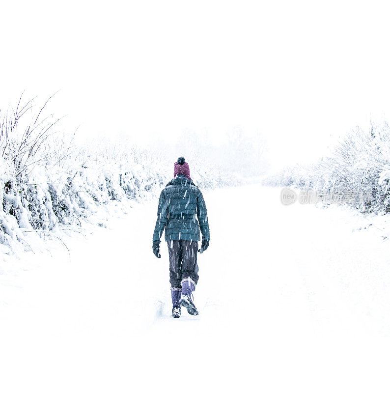 英国科茨沃尔德，格洛斯特郡，赛伦塞斯特公园，一个孤独的女人走在一条被雪覆盖的小路上