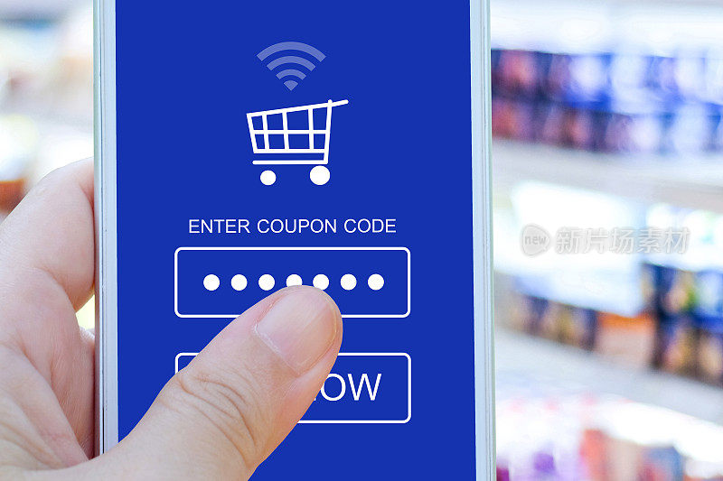 手持智能手机与折扣券代码在屏幕上模糊超市背景，网上购物，商务，电子商务，技术和数字营销背景