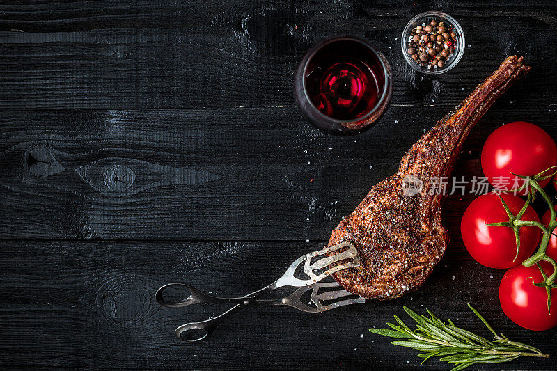烧烤干燥的陈年牛肉肋与香料，蔬菜和一杯红酒特写在黑色木制背景
