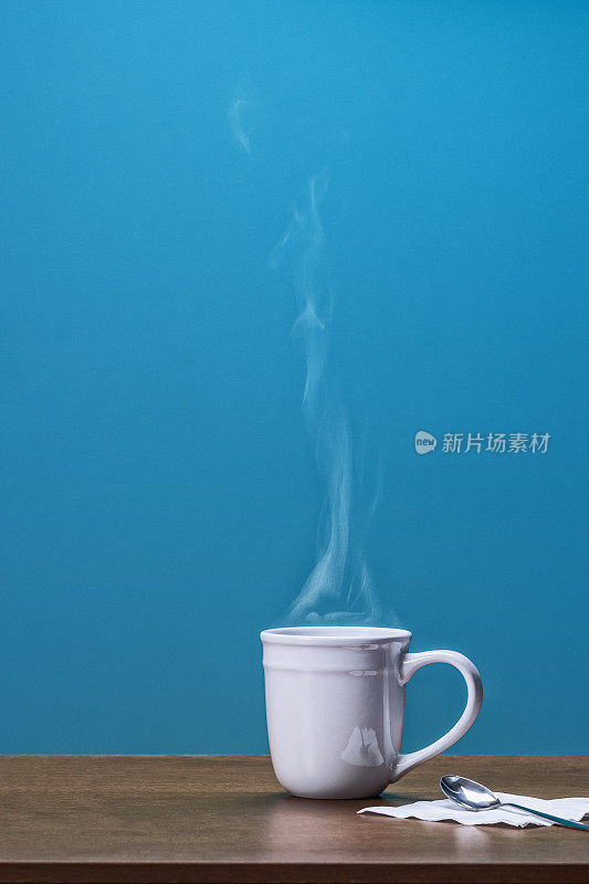 白色的大杯子，上面放着滚烫的咖啡或茶，放置在蓝色墙壁的木桌上