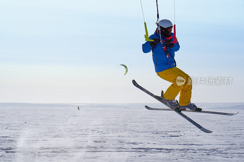一个男运动员正在一个大的雪湖上的冰上放风筝。他跳起来。冬天晴朗有霜的一天。特写镜头。