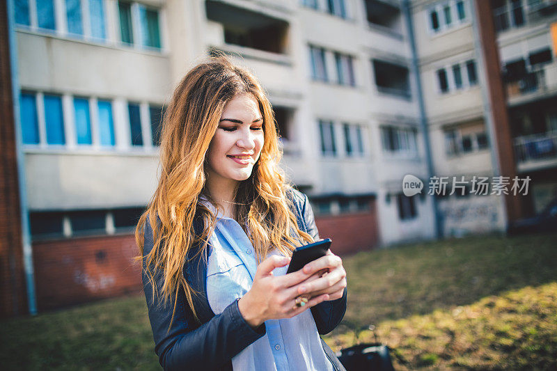 大楼前的女人用手机发短信。