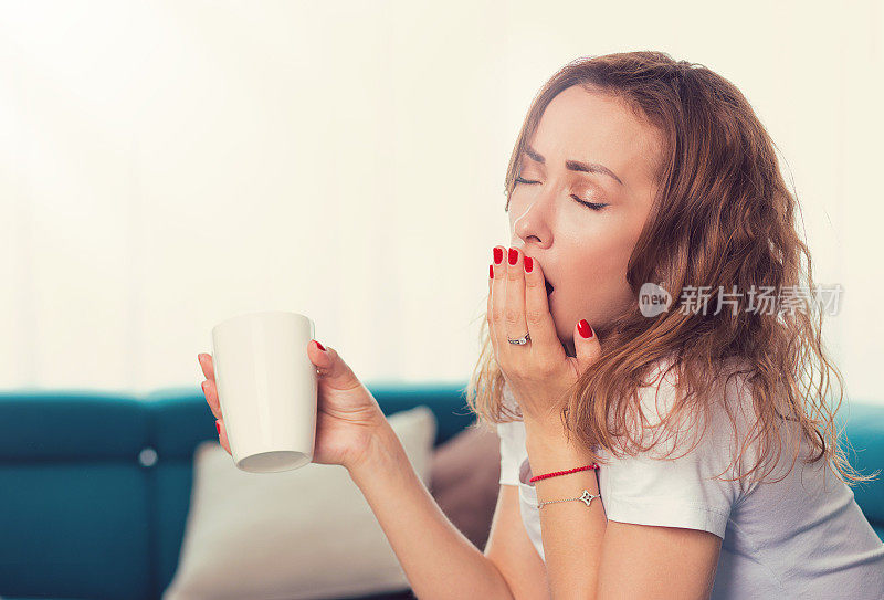 年轻女子坐在沙发上喝着咖啡打呵欠