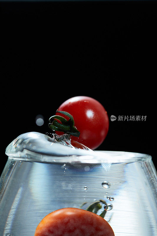 红色圆圆的迷你番茄掉进了玻璃杯的水里，溅起的水花是美丽的