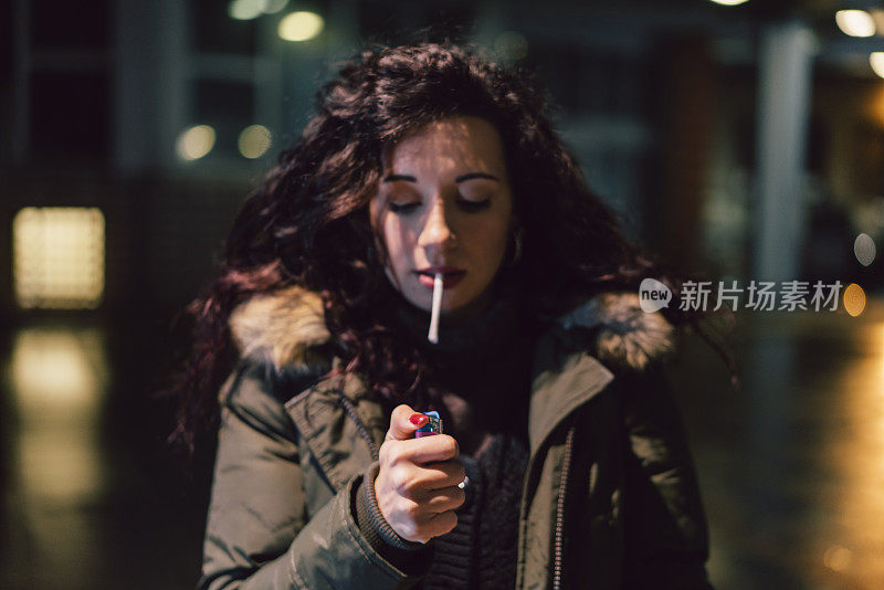 年轻的成年妇女在夜晚的城市里点烟