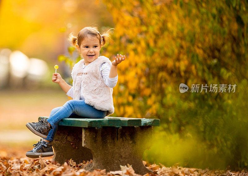 一个阳光明媚的秋日，快乐的小女孩坐在公园的长椅上