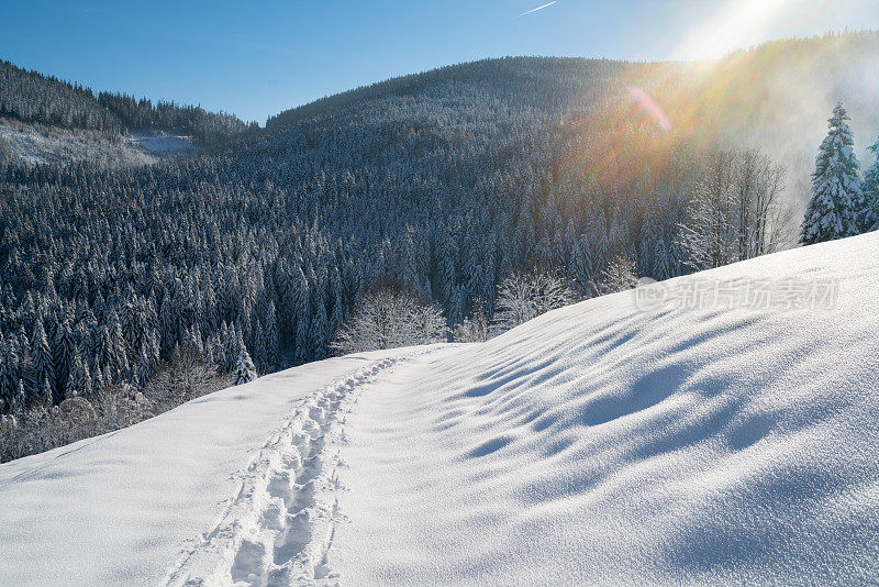 在阳光明媚的冬日里，在多山的乡村景观中，深深的积雪上留下的足迹