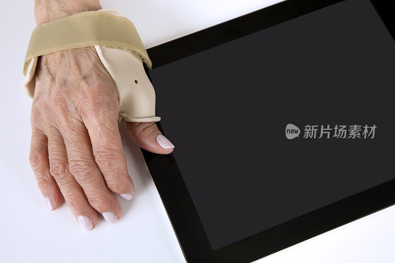 一位老年妇女戴着关节炎支架试图使用平板电脑