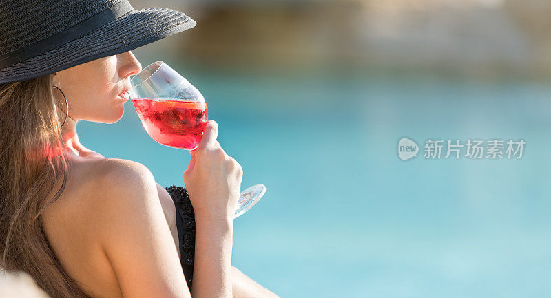 年轻女子穿着比基尼，戴着太阳帽，喝着玫瑰酒