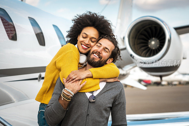 一对浪漫的多文化夫妇在一架私人飞机的机翼旁深情拥抱