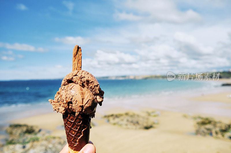 6月的一个阳光明媚的日子里，康沃尔纽基的托万海滩上，手拿着巧克力冰淇淋。