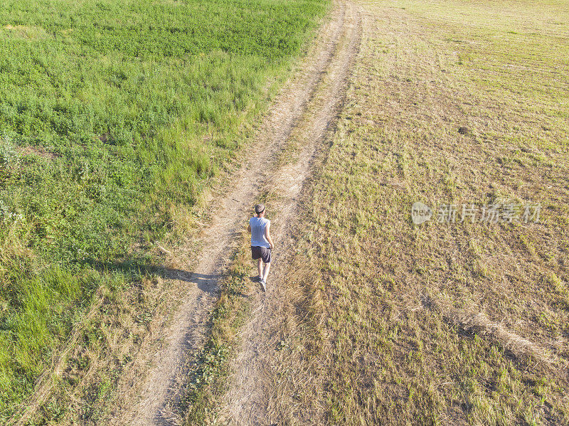 英俊的成年男子慢跑在泥泞的乡村道路穿过草地在阳光明媚的夏天