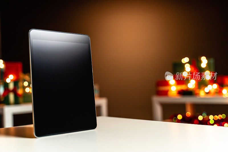 数码平板电脑在白色的桌子前，散焦圣诞灯的背景，散焦