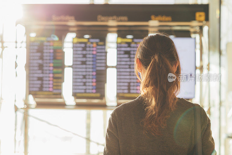 后视图的年轻女子看航班信息板在机场