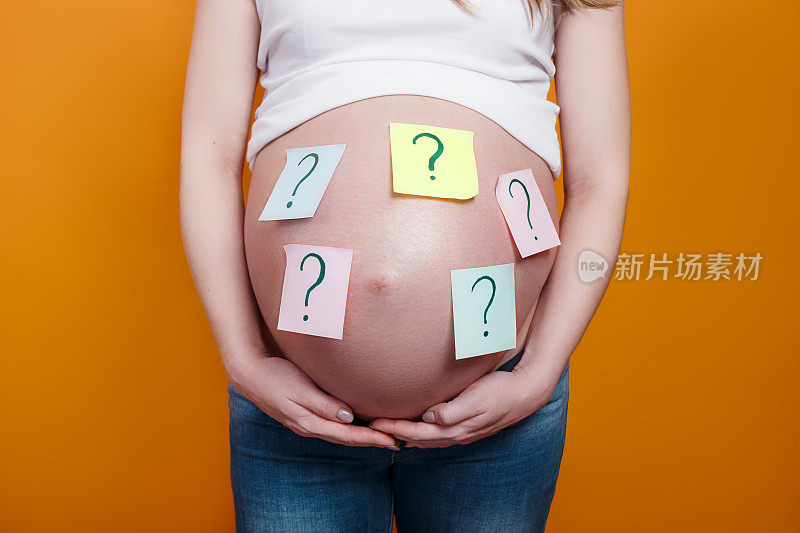 孕妇用黄色的背景纸在肚子上贴上问号