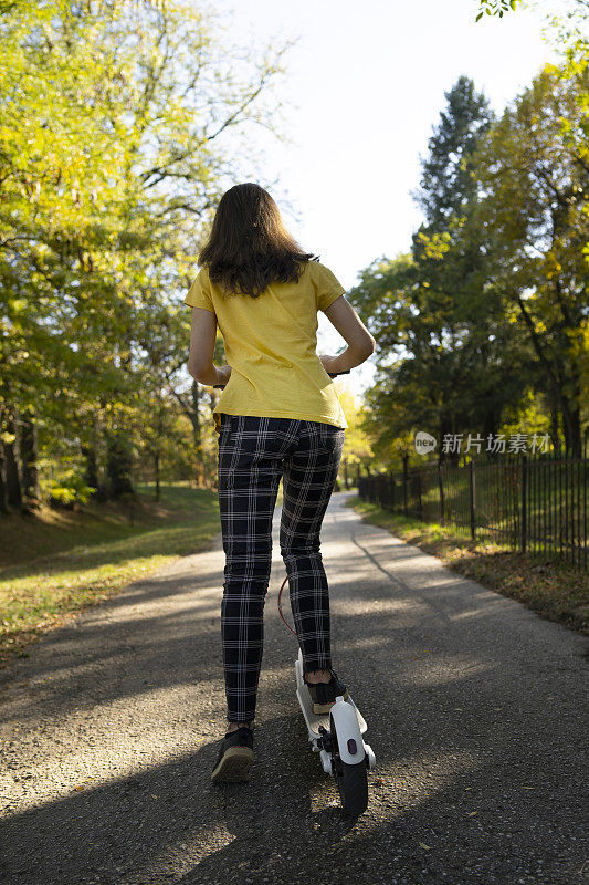 那个女孩在公园的小巷里推着滑板车往前走