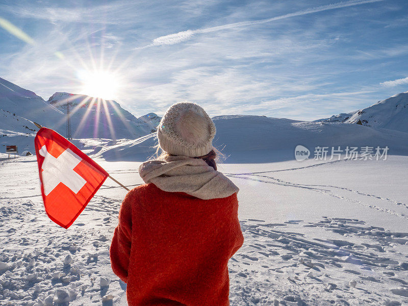 举着瑞士国旗站在瑞士阿尔卑斯山白雪皑皑的山上的女子