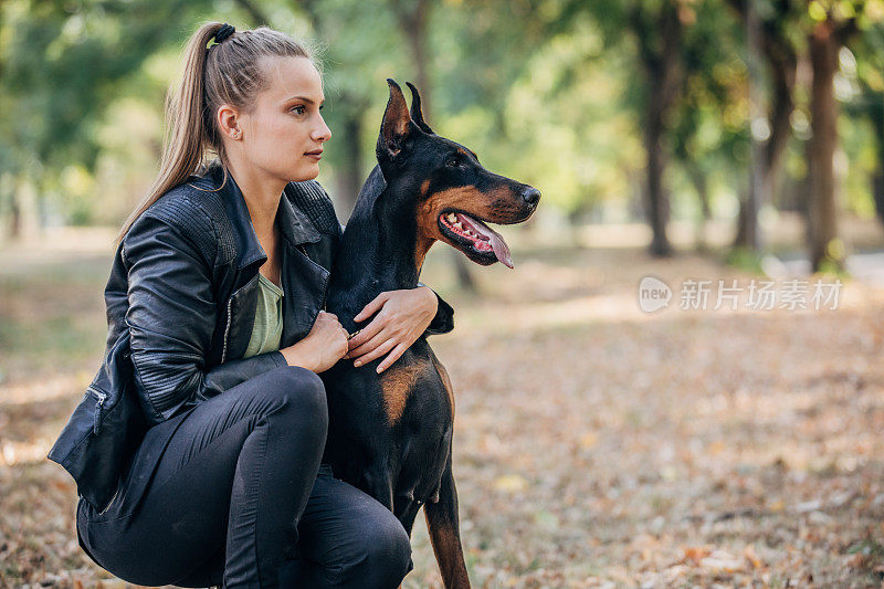 一个年轻女子在公园里和她的杜宾犬玩耍