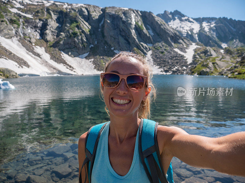 年轻女子在美丽的高山湖周围徒步旅行时自拍