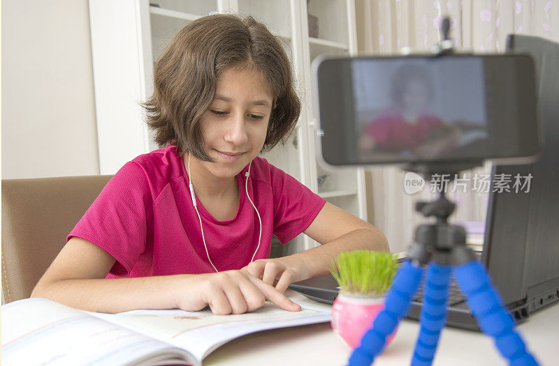 一个十几岁的女孩看书看虚拟课堂在移动由于隔离库存照片