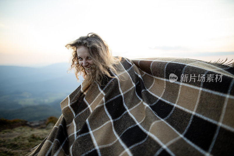 一个漂亮的年轻白种女人正披着花格毯子在秋日的群山中漫步。积极情绪