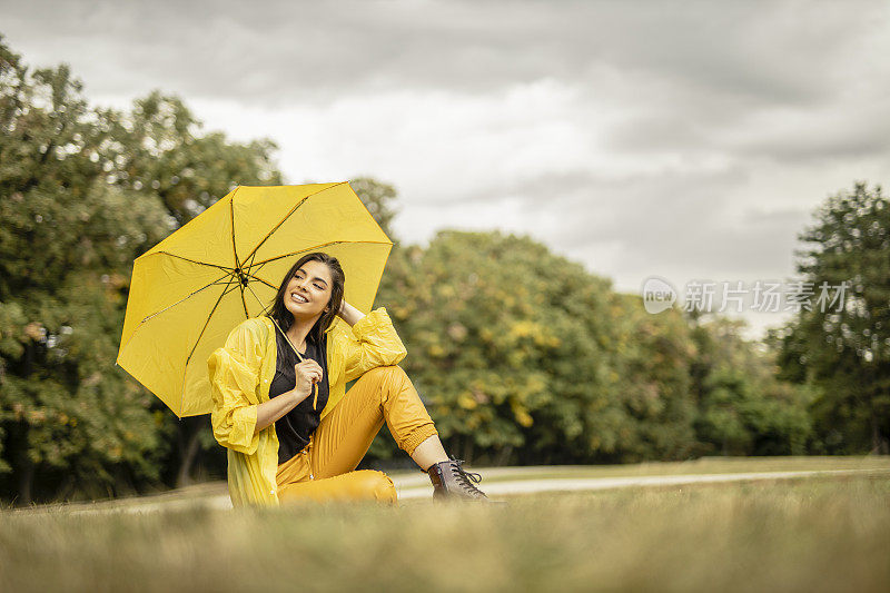 美丽的年轻女子穿着黄色雨衣，拿着黄色雨伞在户外