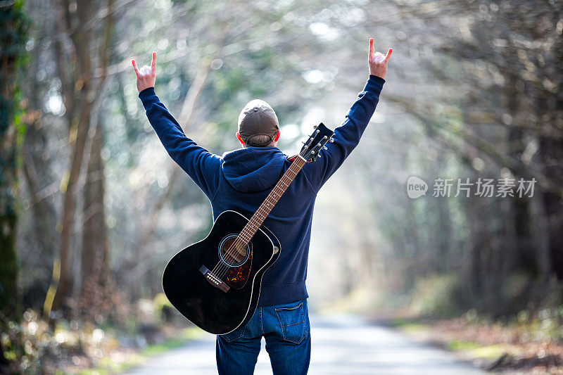 在宽阔的马路上，背着吉他的男人用喇叭做手势