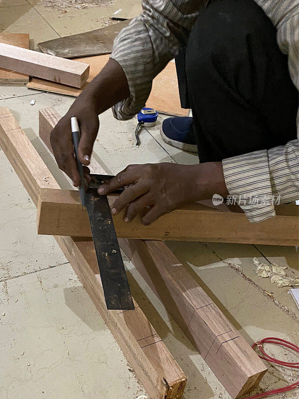 特写图像的印度勤杂工蹲和使用钢，角设置方形在木板上画铅笔线，铺着锯屑的瓷砖地板