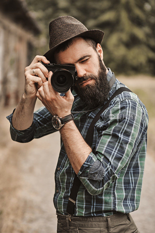 一个留着胡子的英俊的年轻人正在一个绿色的公园里拍照。