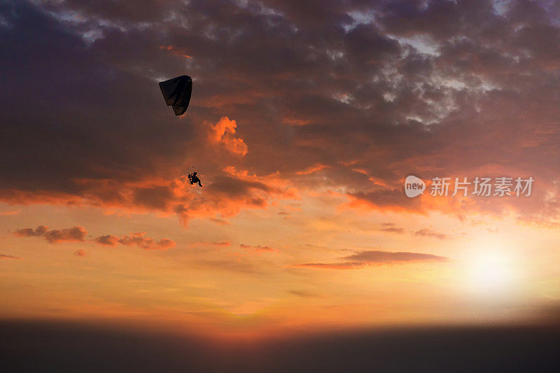 跳伞日落景观降落伞飞行在软焦点。夕阳下的Para-motor飞行剪影。剪影的滑翔伞飞行在傍晚的天空与日落。