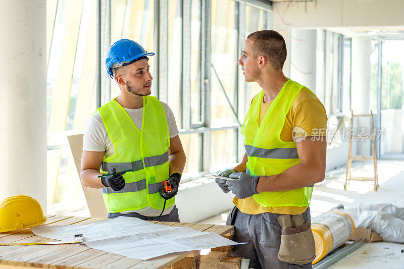 年轻的男性工程师工人领班在室内建筑工地与蓝图