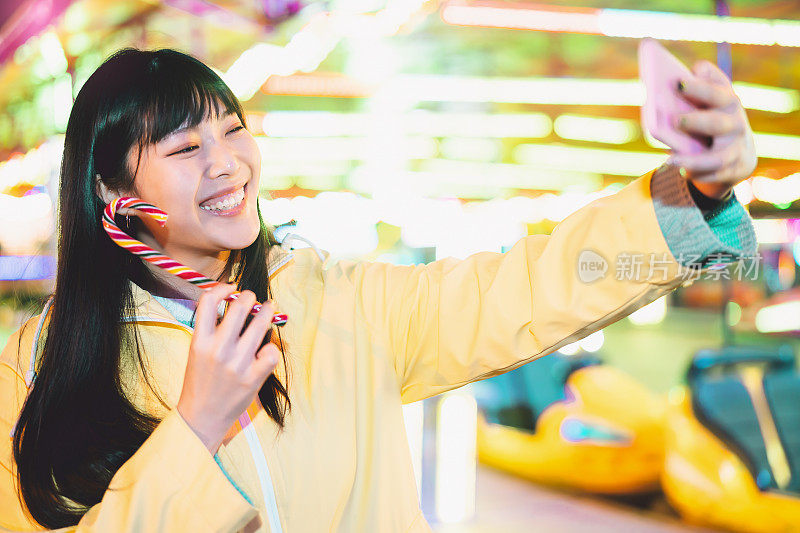 亚洲女孩在游乐园用手机自拍-快乐的女人享受新的趋势智能手机应用程序-青年一代和社交媒体成瘾的概念