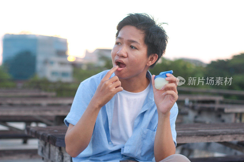 年轻男子坐在户外公园里使用唇部护理