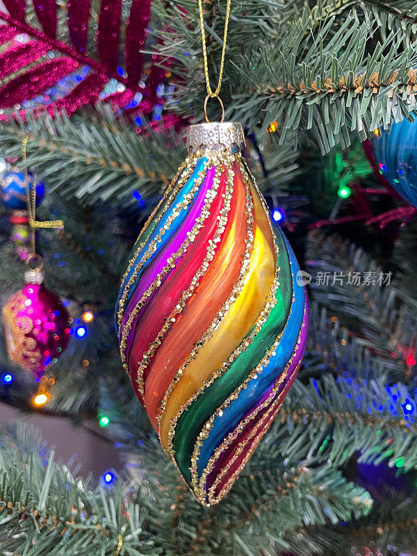 形象的个人，彩虹和闪光的泪珠饰品挂在人造圣诞树的树枝上，云杉针，模糊的多色神仙灯的背景