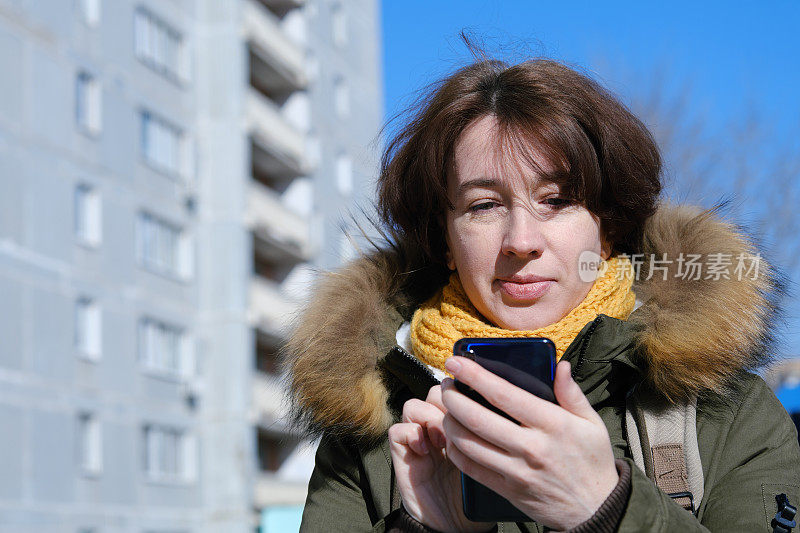 一个穿着暖和衣服的成熟女人在小镇的街道上用手机的肖像