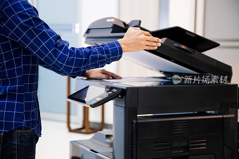 商务人士按下面板上的按钮，便可使用影印机或打印机在办公室打印或扫描文件纸张。