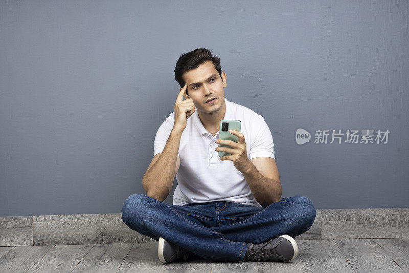 坐在地板上用手机的男人跷着腿，库存照片