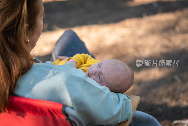 在户外公园里，快乐的年轻母亲和睡着的婴儿坐在一起
