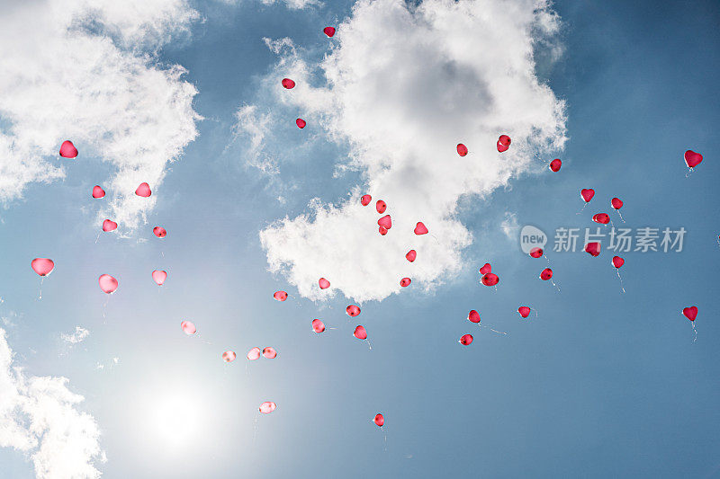 蓝天上飘着几朵云，红色的心形气球正在飞走
