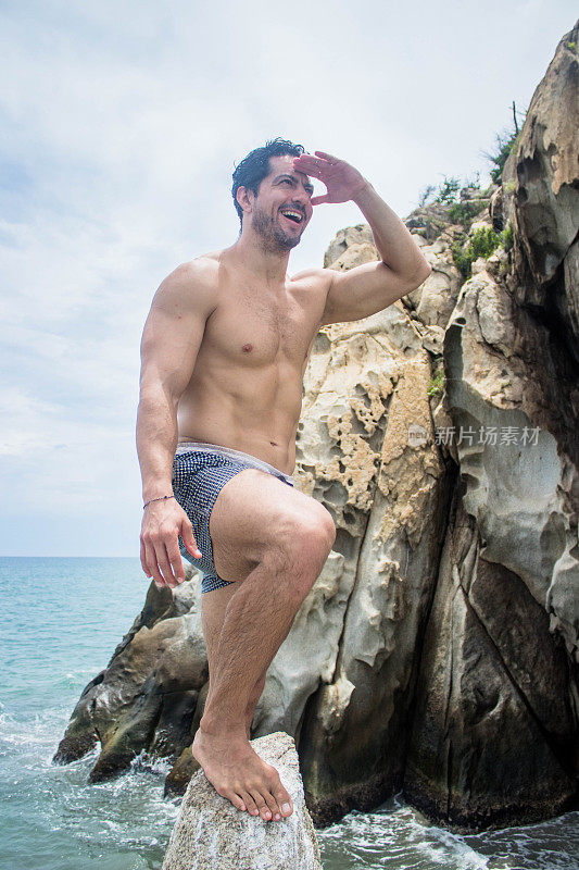 在海滩度假时，一个运动健将的西班牙男子高兴地望着远方的垂直镜头