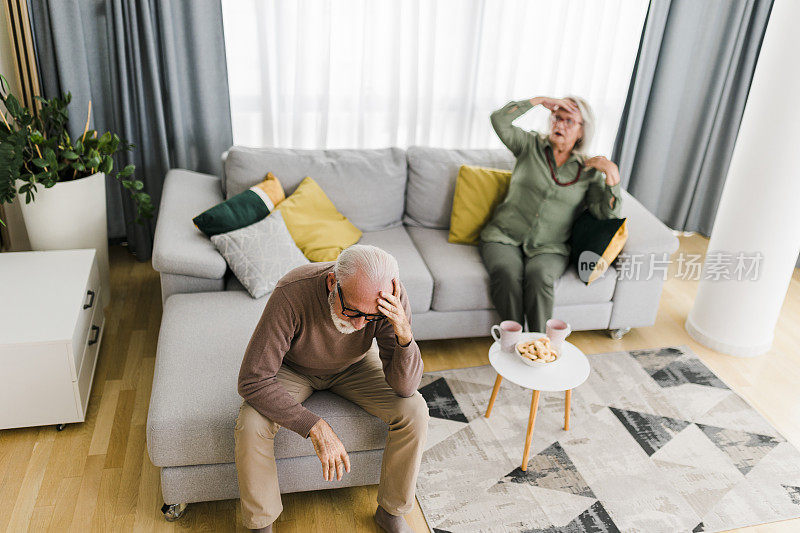 一对年长的异性夫妇坐在家里的沙发上吵架。