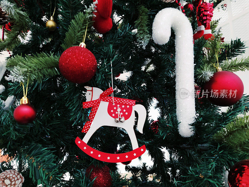 有装饰品、圣诞球和玩具的圣诞树。红白相间的挂饰。漂亮的球，明亮的浆果和球果。雪糖棒。玩具-摇摆马