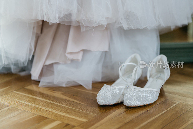 新娘穿着白色的结婚鞋，站在婚纱前的木地板上
