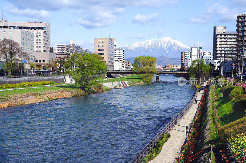 岩手山和盛冈市在北上河滨有建筑和人行道。