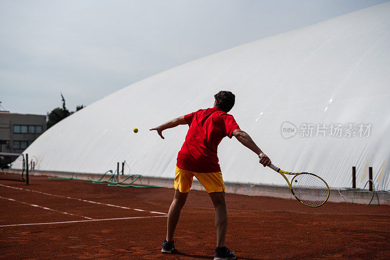 男子网球运动员与红色的t恤是拍正手在红土场上的焦点在前景垂直网球仍然
