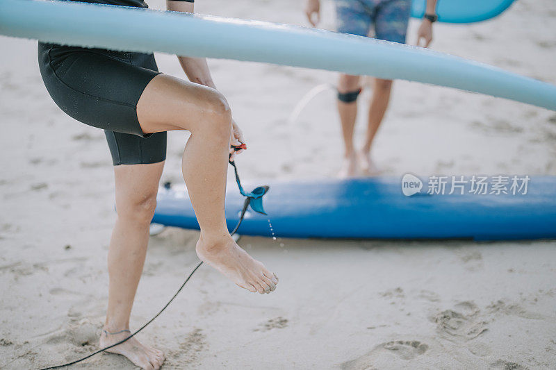 亚洲中国冲浪者在海滩冲浪后解开冲浪板皮带