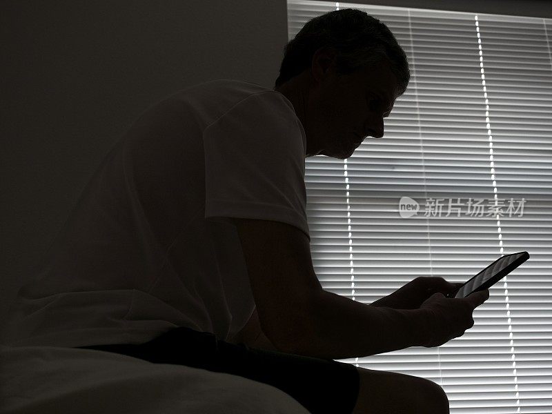 一名男子坐在黑暗的房间里与他的智能手机互动